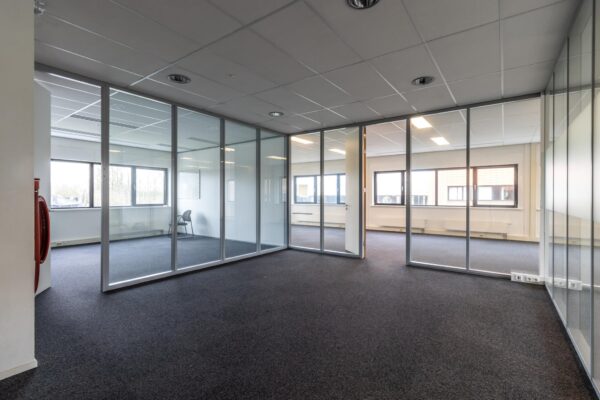 Leeg kantoorpand aan de Lage Biezenweg met glazen scheidingswanden en uitzicht op buiten.